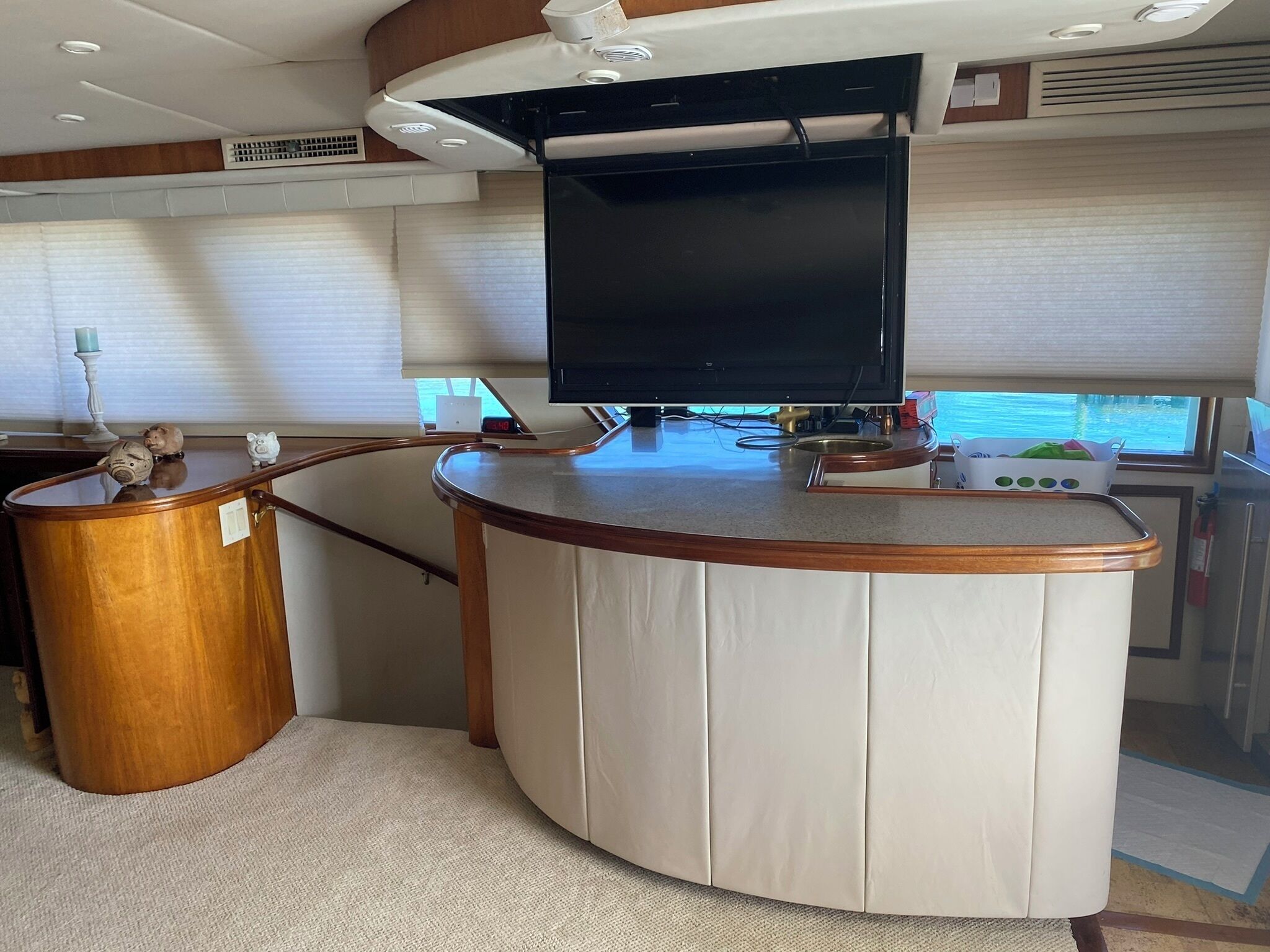 Un espace de vie compact doté d’un bar en bois aux lignes courbes, d’un téléviseur à écran plat fixé au-dessus, et d’une petite tirelire posée sur le bar.