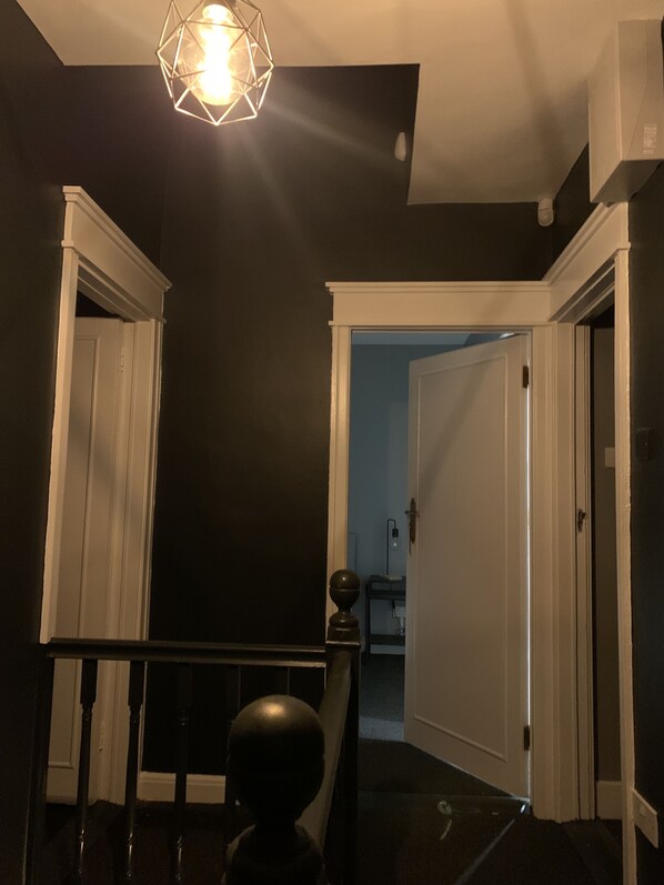 A dark room with a geometric light fixture, a white door, and a staircase leading to another room.