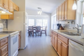A modern kitchen with wooden cabinets, a built-in oven, a refrigerator, and a dining area with chairs and a table. - Escape to Tranquility at Whispering Woods Cottage (Haliburton)