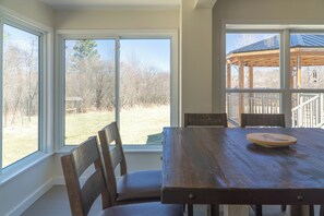 A dining area with a wooden table and chairs, large windows offering a view of the outdoors. - Escape to Tranquility at Whispering Woods Cottage (Haliburton)