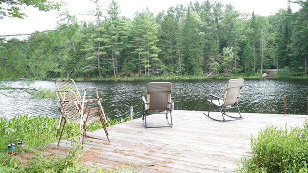 A wooden dock with two chairs facing a calm lake surrounded by dense forest.