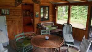 A cozy cabin interior with wicker furniture, a dining table, and a view of the forest.