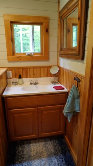 Un baño de madera con ventana, lavamanos, espejo y toallero.