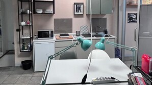 A modern kitchen with a white countertop, two pendant lights, a teal desk lamp, and a refrigerator.