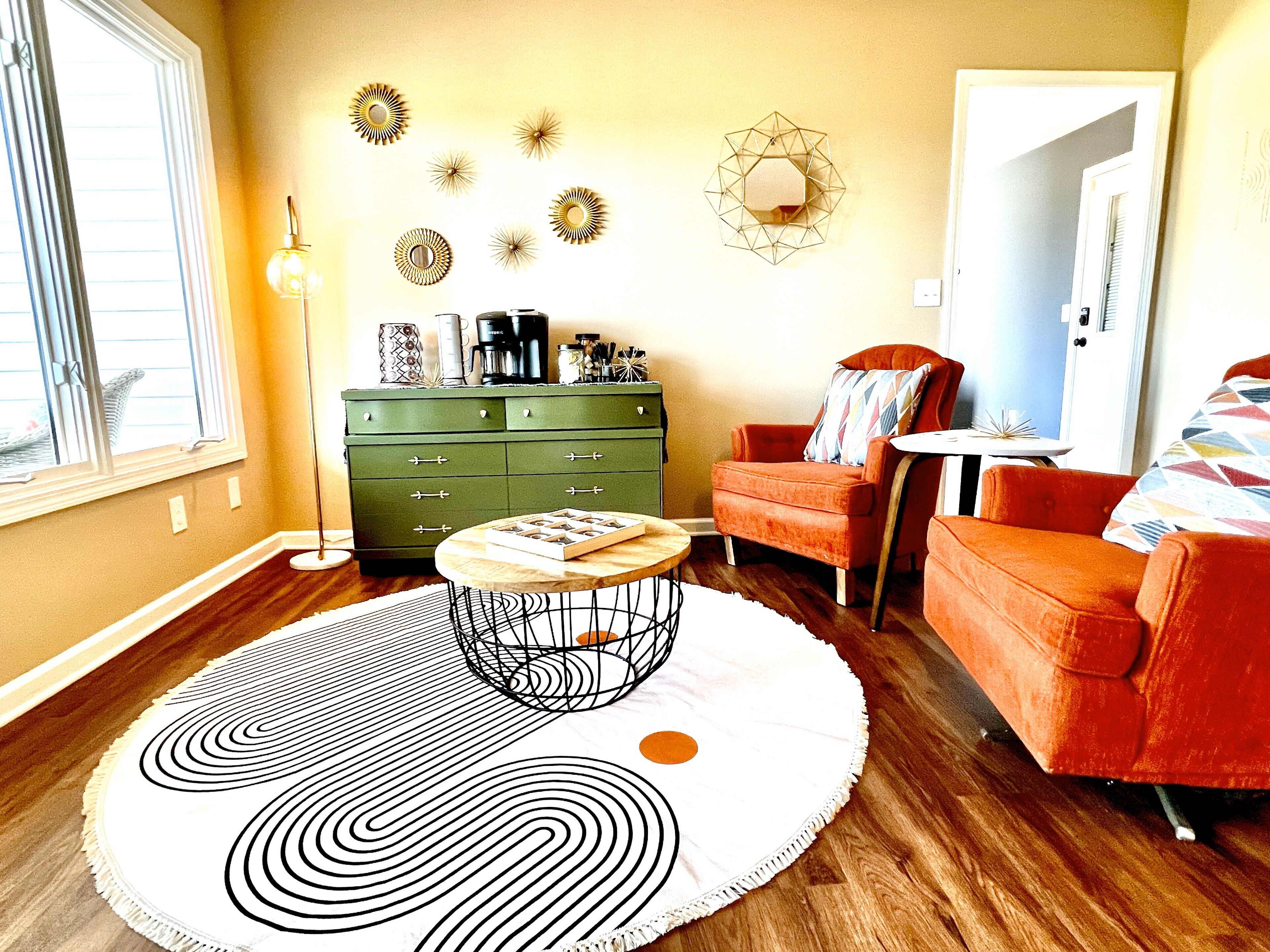 Un salon avec une commode verte, une table basse ronde et deux fauteuils orange.