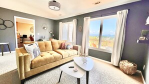 A modern living room with a beige sofa, a round coffee table, and a large window offering a city view. - Iconic Dahlonega View! In Town! WINE GOLD HIKING (Dahlonega)