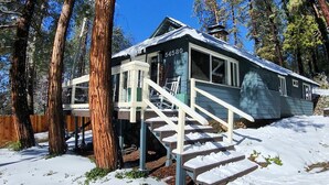 Eine Holzhütte mit einer Treppe, die zu einer Terrasse führt, umgeben von hohen Bäumen und bedeckt mit Schnee.