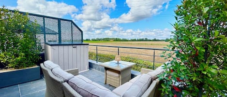 Un patio con mobiliario de mimbre, una mesita y vistas a un campo.
