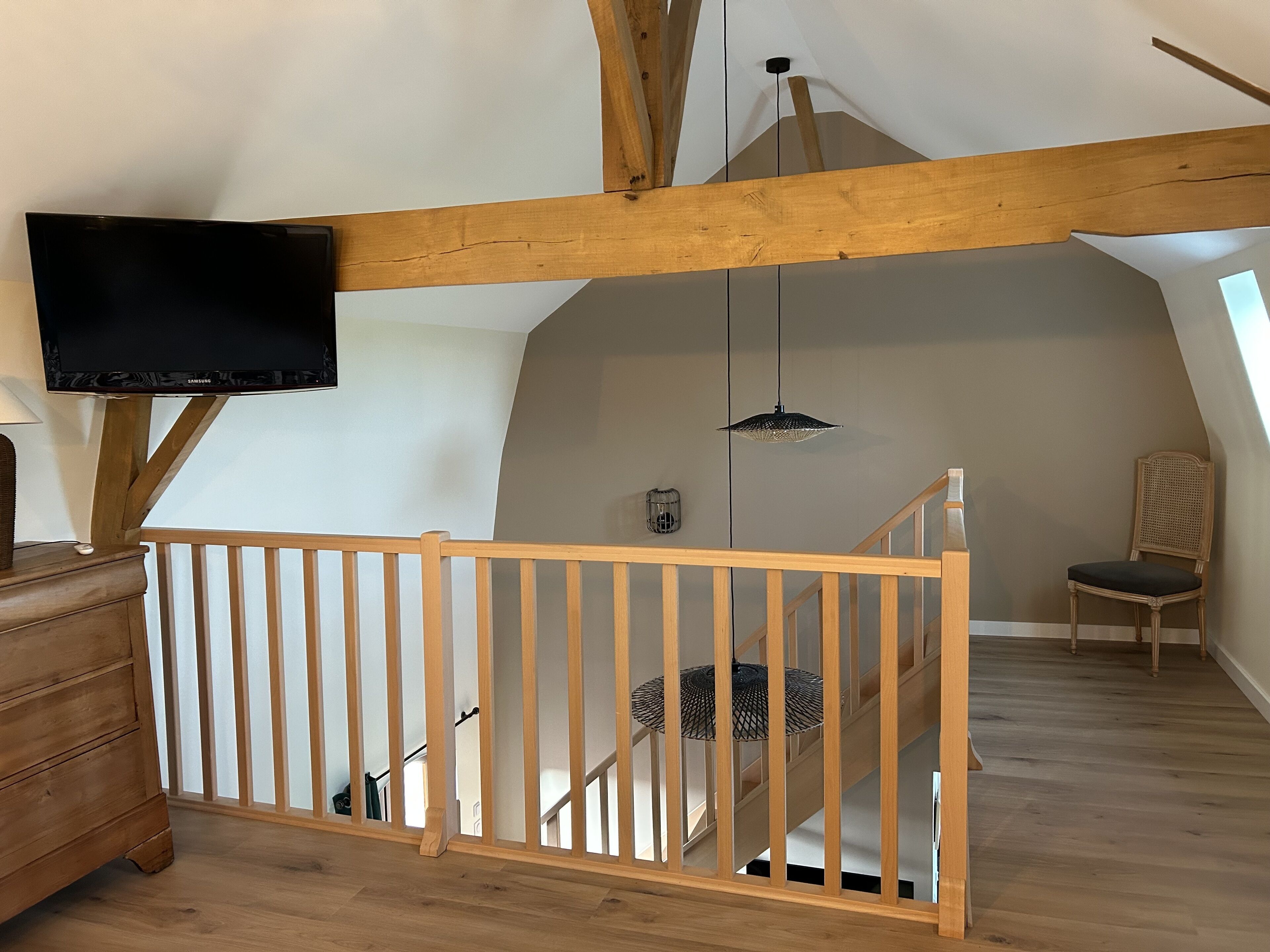 A loft-style room with wooden beams, a TV mounted on the wall, a staircase, and a chair.
