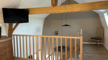 A loft-style room with wooden beams, a TV mounted on the wall, a staircase, and a chair.
