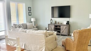 A living room with a sofa, a wicker chair, a TV, and a ceiling fan. - Pensacola Beach - 4 Bedrooms w/ Beach and Pool Access! (Pensacola Beach)