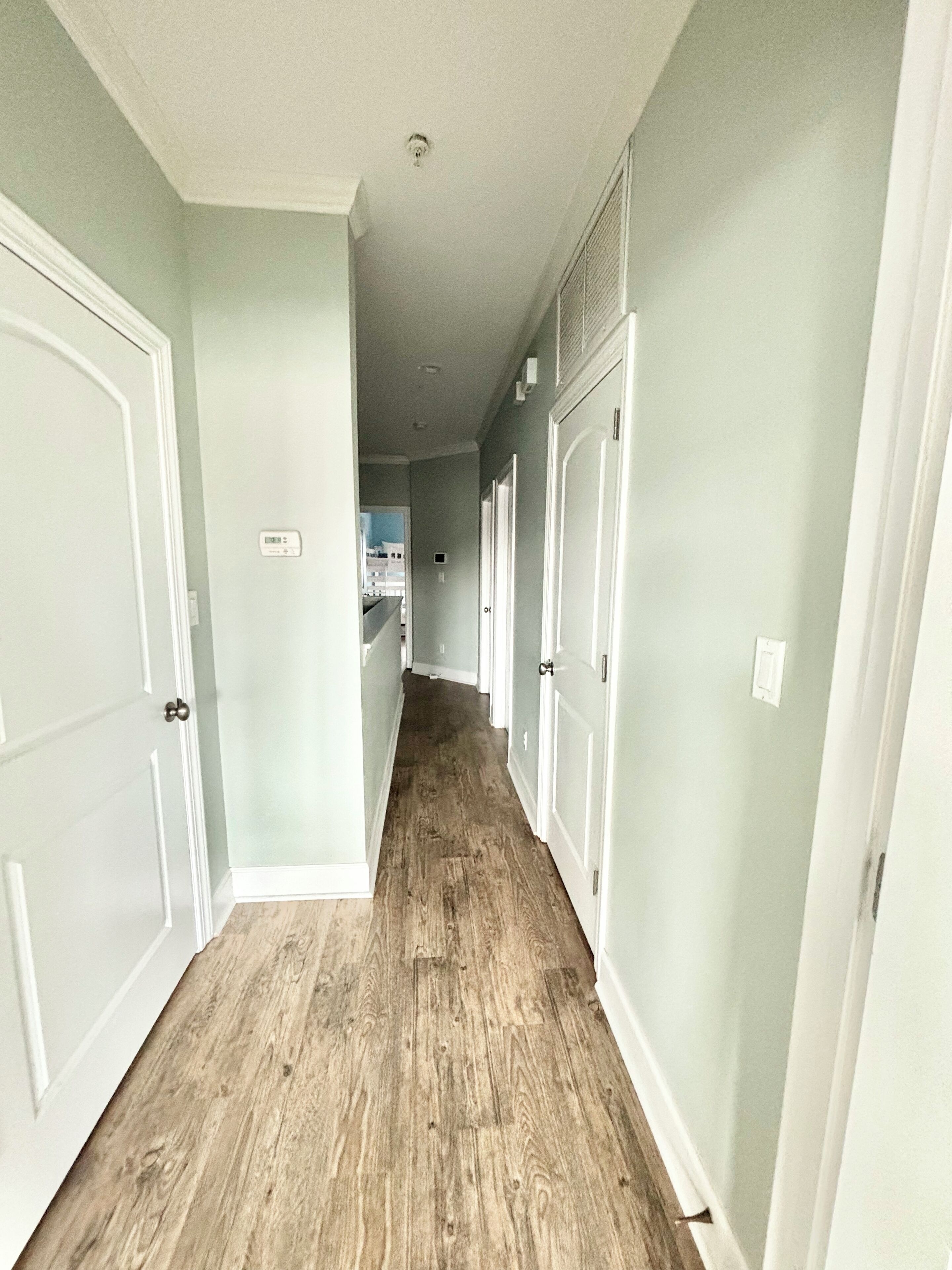 A hallway with light green walls, white doors, and wooden flooring.