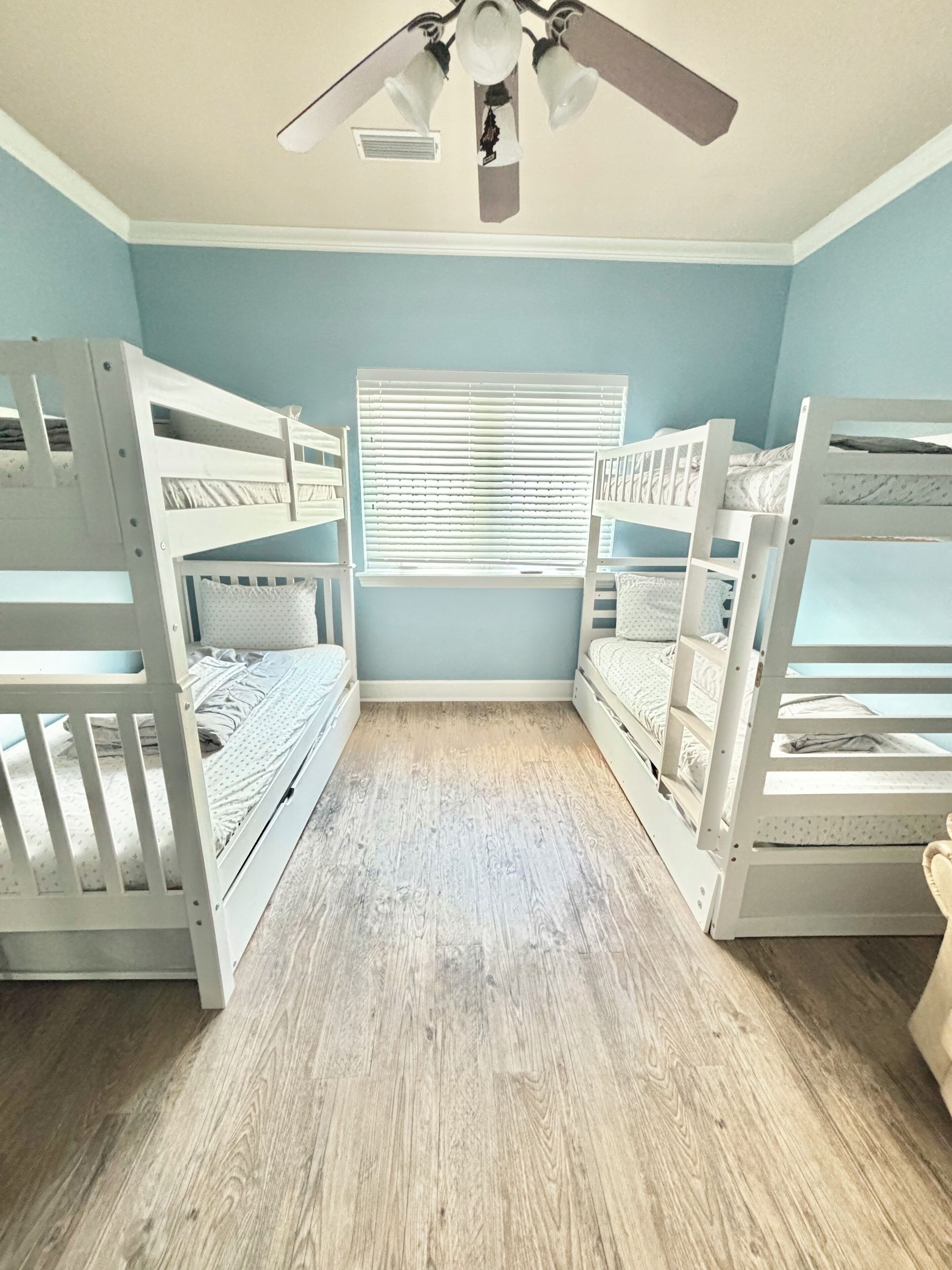 A room with bunk beds, a ceiling fan, and a window with blinds.