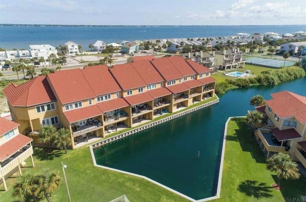 A multi-story hotel with a red roof, a pool, and a view of the sea.