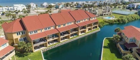 A multi-story hotel with a red roof, a pool, and a view of the sea.