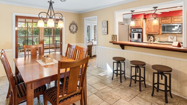 A dining area with a wooden table and chairs, a kitchen with wooden cabinets and a microwave, and a view of the outdoors through a glass door. - Timber View Retreat-Large 4 BR close to shopping & restaurants in NE Longview (Longview)