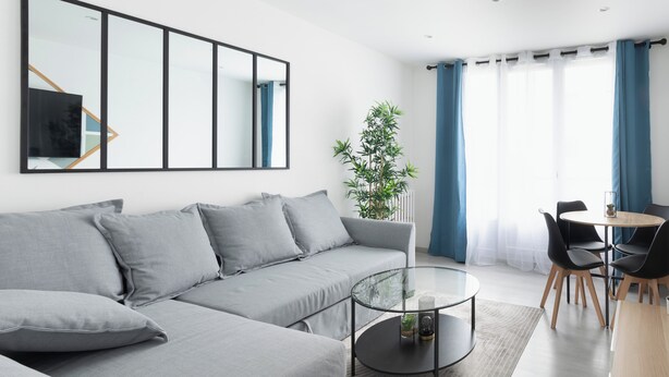 A modern living room with a grey sofa, a glass coffee table, and a dining area with a round table and chairs.