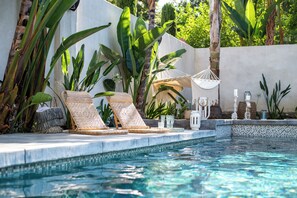 Ein Poolbereich mit Liegestühlen, einer Hängematte und tropischer Bepflanzung.