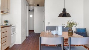 Une cuisine avec des meubles blancs, un sol en briques et un coin repas comprenant une table, des chaises et un luminaire suspendu.