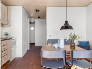 A kitchen with white cabinets, a brick floor, and a dining area with a table, chairs, and a hanging light fixture.
