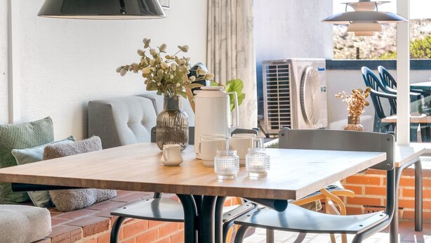 Un espace repas comprenant une table, des chaises, un vase avec des fleurs et un luminaire suspendu.