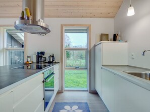 A modern kitchen with a built-in oven, a coffee maker, and a view of a green landscape through a large window.