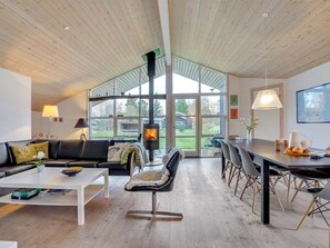 A spacious living area with a high ceiling, a fireplace, a dining table with chairs, and a view of the outdoors. - "Elni" - 900m from the sea by Interhome (Hals)