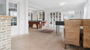 Un vaste espace de vie comprenant une table de billard, une bibliothèque et des meubles en osier.