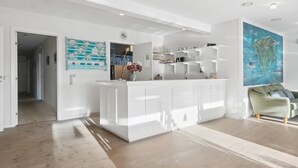 Une cuisine moderne avec des meubles blancs, un îlot central et un coin repas agrémenté d’un canapé vert.