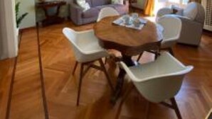 Un comedor con una mesa redonda y sillas blancas, una lámpara de araña y un sofá al fondo.