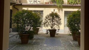 Un patio con plantas en macetas, piso de baldosas y un edificio con techo y balcones a ladrillo.