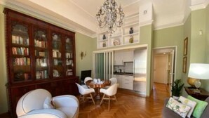 Una sala de estar con un sofá, una mesa de comedor con sillas, una estantería y una araña.