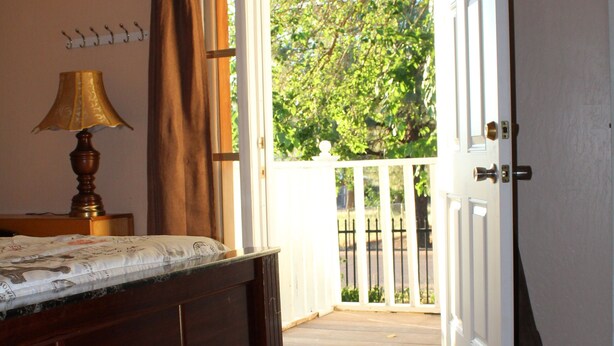 Une chambre à coucher comprenant un lit, une table de chevet, une lampe et donnant sur un balcon avec une balustrade en bois.
