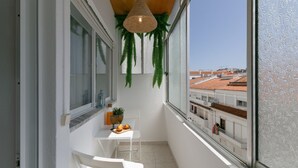 Ein Balkon mit einem weißen Tisch, Stühlen, einer hängenden Pflanze und Blick auf Gebäude.