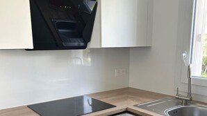 A modern kitchen with white cabinets, a black dishwasher, a built-in oven, a stainless steel sink, and a window providing natural light. - RENECROS 1 à 30 m de la mer Very Large Terrace Wifi Clim Parking (BANDOL)