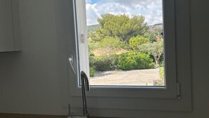 A kitchen with a stainless steel sink and a window overlooking a green landscape. - RENECROS 1 à 30 m de la mer Very Large Terrace Wifi Clim Parking (BANDOL)