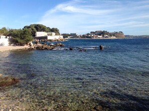 Ett kustområde med klart vatten, en stenig strand och byggnader på sluttningen.