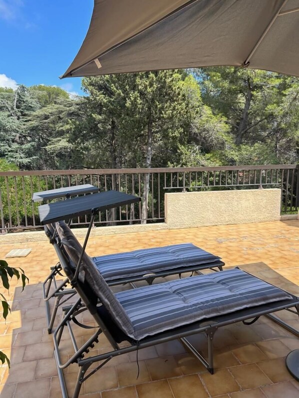 A patio with two lounge chairs and a table under a large shade sail.