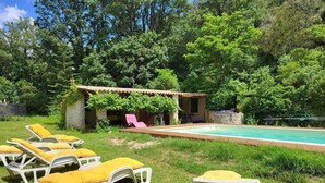 A pool area with lounge chairs and a small building with a roof.