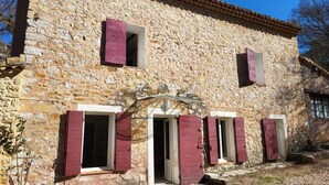 A stone building with three windows, each with red shutters, and a small porch area.