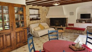 A cozy living room with a stone fireplace, wooden beams, a TV, and a dining area with a table and chairs.