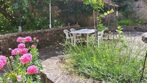A stone patio with a table and chairs, surrounded by greenery and flowering plants.