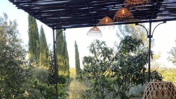 A wooden table with a bowl, surrounded by chairs, under a pergola with hanging lights. - La Rouvraie - FLAYOSC (FLAYOSC)