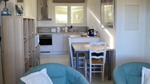 A compact living space with a kitchenette, two teal armchairs, a dining table with chairs, and a large window providing natural light. - La Rouvraie - FLAYOSC (FLAYOSC)