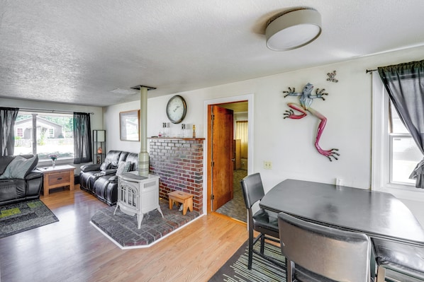 A living room with a fireplace, a dining table with chairs, and a kitchen area visible through an open door.