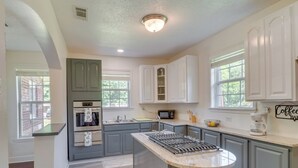 A kitchen with a central island, built-in appliances, and a window providing natural light. - Renovated Louisiana Rental Near Mississippi River (Ferriday)