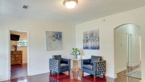 A spacious room with hardwood flooring, two leather armchairs, a small round table with a vase of flowers, and artwork on the walls. - Renovated Louisiana Rental Near Mississippi River (Ferriday)