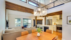A modern kitchen with stainless steel appliances, a wooden dining table, and a large window overlooking the outdoors. - Walk to Main St & Lifts: Ketchum Townhouse! (Ketchum)