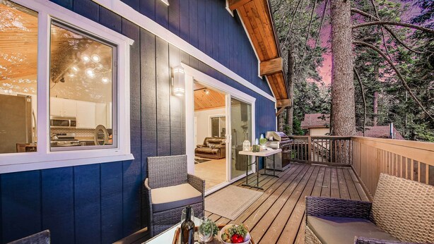 A deck with wicker furniture, a dining table, and a bottle of wine. - Tree-Lined Lake Arrowhead Cabin ~ 1 Mi to Village! (Lake Arrowhead)