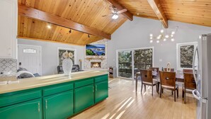 A modern kitchen with green cabinets, wooden ceiling beams, and a dining area with a large window. - Tree-Lined Lake Arrowhead Cabin ~ 1 Mi to Village! (Lake Arrowhead)